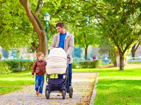 Vater mit Kind an der Hand und Kinderwagen im Park