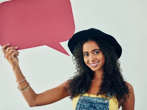 Junge BIPOC Frau hält lächelnd Sprechblase hoch