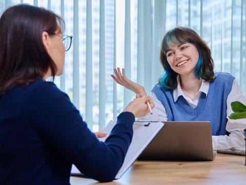 Eine Lehrerin mittleren Alters, Mentorin im Gespräch, hilft dabei, Teenager-Studentinnen zu testen, die im Büro im College-Gebäude sitzen. Bildung