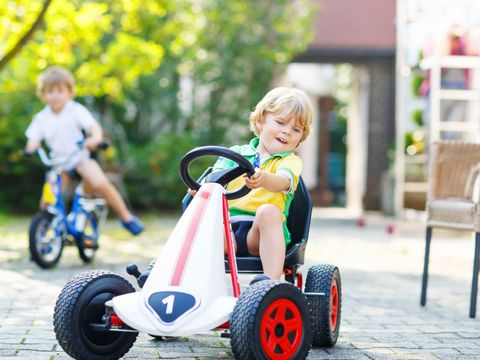 Kleines Kind Junge Tretauto im Sommergarten fahren