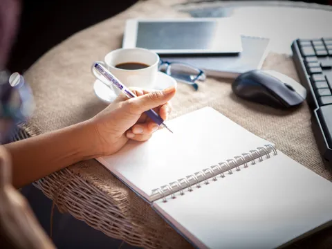 Hand, die am Tisch schreibt mit Tastatur, Maus, Tablet, Kaffeetasse