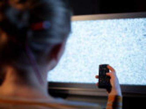 Frau mit Fernbedienung vor einem Fernseher