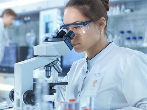 Wissenschaftlerin schaut durch ein Mikroskop