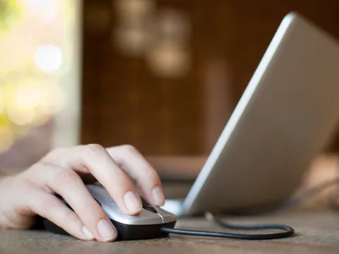 Hand auf der Maus neben einem Laptop