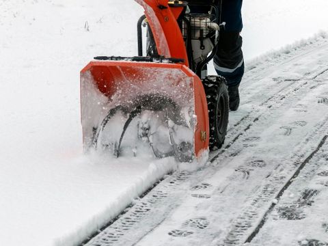 Ein Mann arbeitet mit einer Schneefräse, um frisch gefallenen Schnee von einer Hochspannungstransformator-Einfahrt zu entfernen