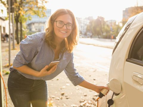 Frau steht am Elektroauto mit Smartphone in der Hand