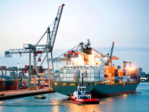 Ein riesiges Containerschiff wird von Lotsen und Schleppern manövriert und rückwärts in Richtung Land gebracht.