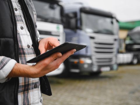Mann mit digitalem Tablet, das den Flottenbetrieb und die Frachtlogistik steuert, steht in der Nähe einer Reihe von Transportfahrzeugen