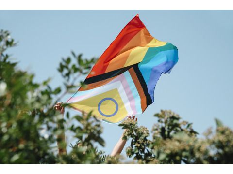 progressive pride flagge wird von zwei Händen gehalten vor blauem Himmel