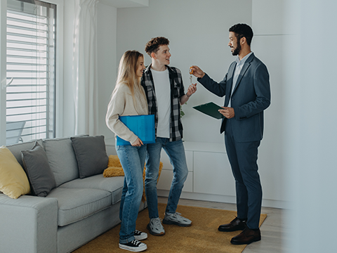 Glückliches junges Pärchen bei der Schlüsselübergabe Ihrer neuen Wohnung durch einen Makler