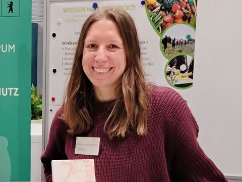 Mitarbeiterin des FÖL e.V. steht an einem Stand mit Informationsmaterial auf der Grünen Woche 2025