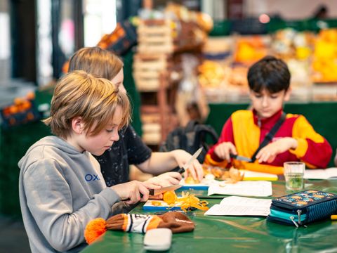 drei Kinder sitzen gemeinsam an einem Tisch und schneiden Gemüse