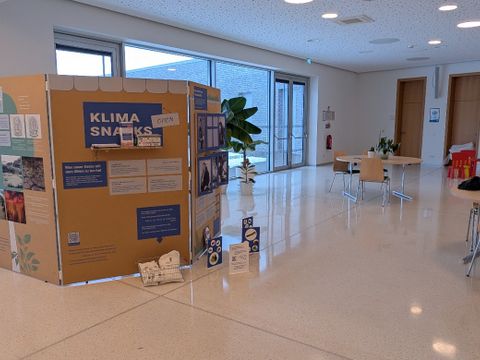 Eine Ausstellungswand zeigt viele verschiedene Bilder und Texte, zu lesen ist die große Überschrift "Klima Snacks"
