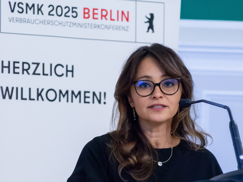 Senatorin für Verbraucherschutz Dr. Felor Badenberg steht an einem Rednerpult, im Hintergrund ist auf einem Banner zu lesen " VSMK 2025 Berlin Herzlich Willkommen"