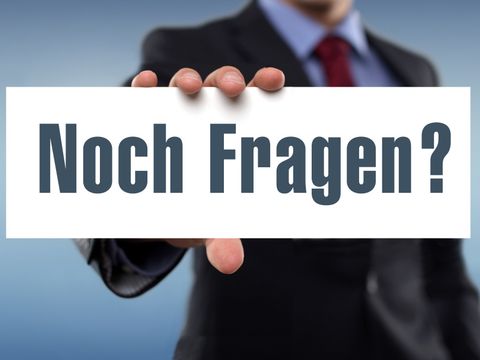 Eine Person hält ein Schild mit dem Text "Noch Fragen?" hoch