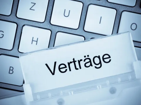 Akte mit dem Reiter "Verträge". Im Hintergrund liegt eine PC-Tastatur.