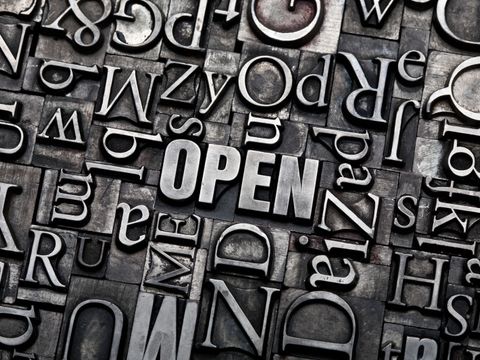 Wort "Open" zusammengesetzt aus Bleilettern, mit vielen weiteren Buchstaben im Hintergrund