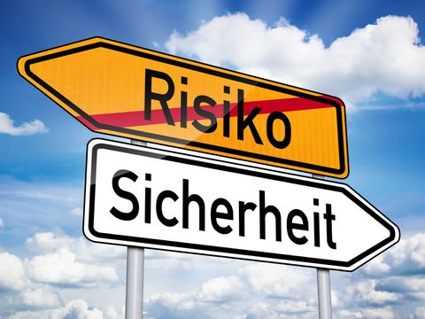 Zwei Verkehrsschilder, die in entgegengesetzte Richtungen zeigen. Auf dem einem Schild steht das durchgestrichene Wort "Risiko"; auf dem anderen das Wort "Sicherheit"