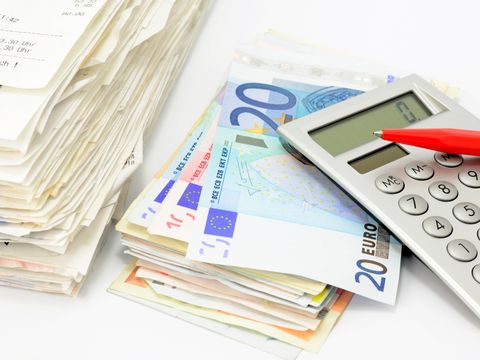 Das Bild zeigt einen Rechnungs- und einen Geldstapel mit Taschenrechner und Stift