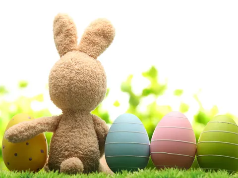 Plüschosterhase von hinten sitzt auf einer Wiese neben bunten Ostereiern