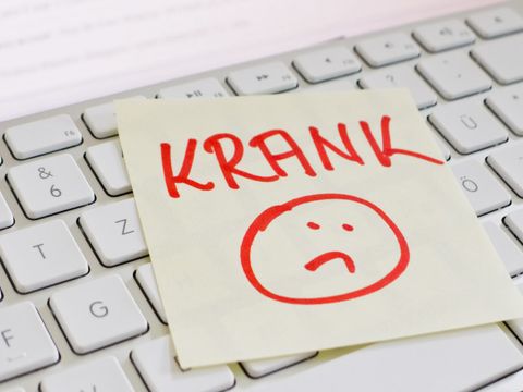 Eine Computertastatur auf der ein gelber Notizzettel liegt mit der Aufschrift KRANK und einem traurigen Gesicht in roter Schrift