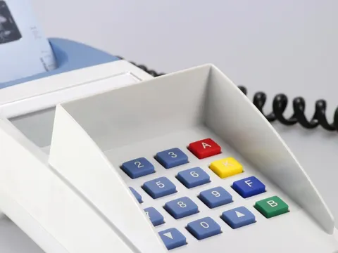 Kleines graues elektronische Gerät zur elektronischen Bezahlung mit Geldkarte und schwarz gekringelten Stromkabel auf weißem Hintergrund