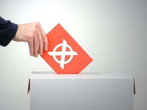 Hand, die einen Umschlag in eine Wahlurne steckt