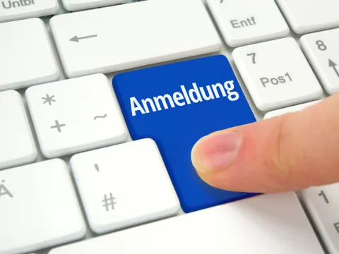 Zeigefinger wählt blaue Anmelde-Taste auf einer Tastatur aus