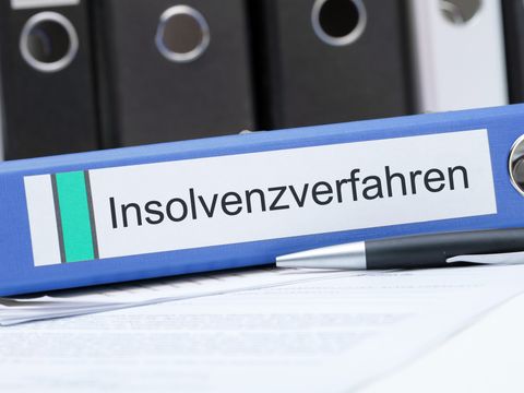 Ein Stift und ein Aktenordner mit der Aufschrift 'Insolvenzverfahren' liegen vor einer Reihe weiterer Ordner