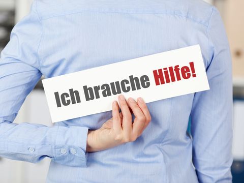 Eine Frau hält hinter ihrem Rücken ein Schild mit der Aufschrift 'Ich brauche Hilfe'