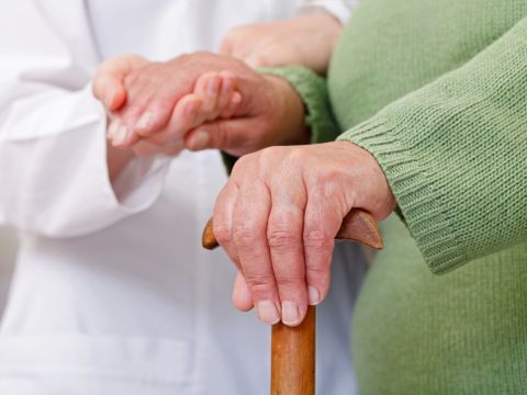 Bildausschnitt Arzt hält Hand von Seniorin mit Krückstock