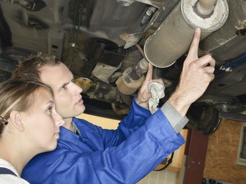 Auszubildende beim Prüfen einer Abgasanlage in einer Kfz Werkstatt