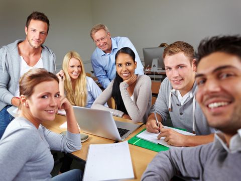 Gruppe von Studenten um einen Tisch mit Lernmaterialien lacht in die Kamera