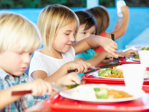 Grundschüler sitzen an einem Tisch und essen gemeinsam Mittag