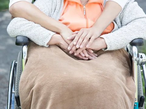 Frau im Rollstuhl wird von hinten umarmt