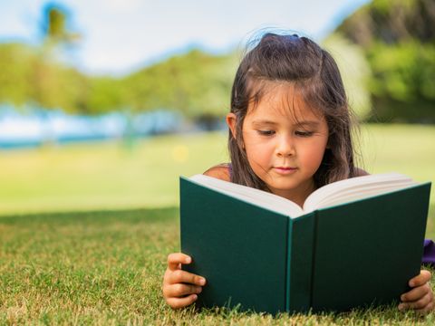 Mädchen liegt auf einer Wiese und liest ein Buch