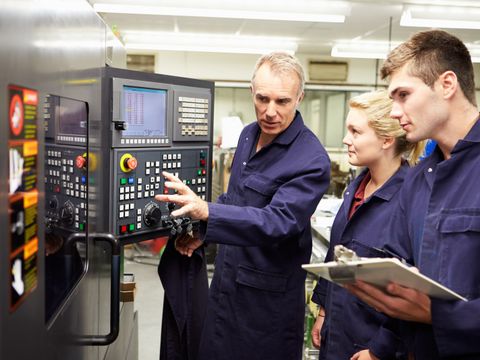 Ingenieur, der Lehrlingen die Verwendung einer computerisierten Drehbank zeigt