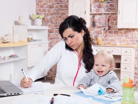 Mutter mit Kleinkind am Schreibtisch bei der Arbeit zu Hause