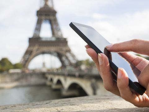 Hand hält Smartphone, im Hintergrund Eiffelturm