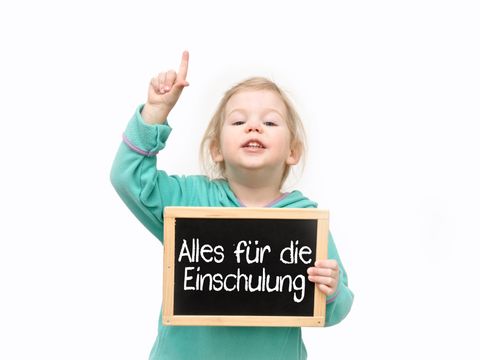 Blondes Mädchen mit einer Tafel in der Hand, auf der Steht "Alles für die Einschulung"