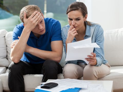 Ein Mann und eine Frau sitzen auf einem Sofa und sehen sich besorgt mehrere Dokumente an