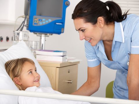 Krankenschwester steht am Krankenbett eines lächelnden Mädchens