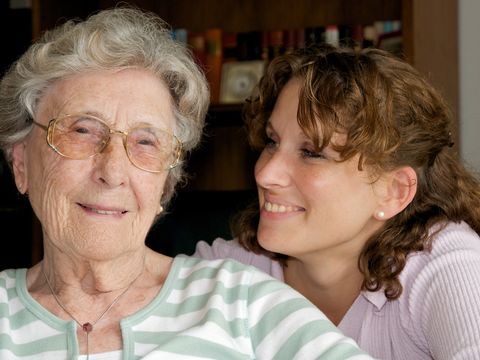 Junge Frau sitzt an der Seite einer Seniorin und lächelt sie an