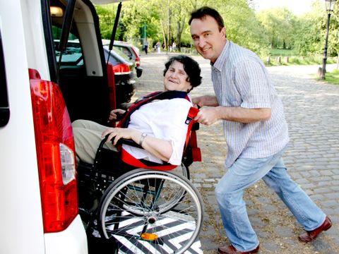 Mann schiebt Rollstuhlfahrerin in ein Auto