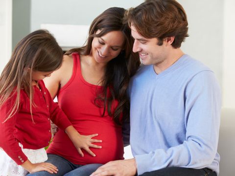 Mädchen legt Hand auf den Babybauch seiner Mutter