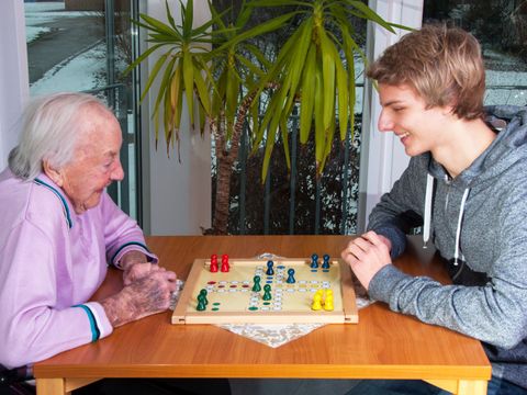 Ein Jugendlicher spielt mit einer Seniorin ein Brettspiel