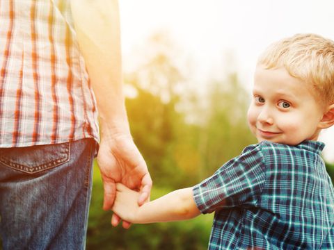 Junge an Hand seines Vaters lächelt in die Kamera