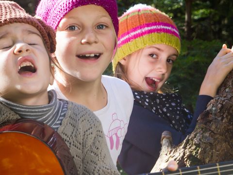 Drei Mädchen sitzen auf einem Baumstamm und singen und spielen Gitarre