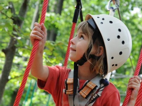 Ein Mädchen mit Schutzhelm und Sicherungsseil klettert im Seilgarten