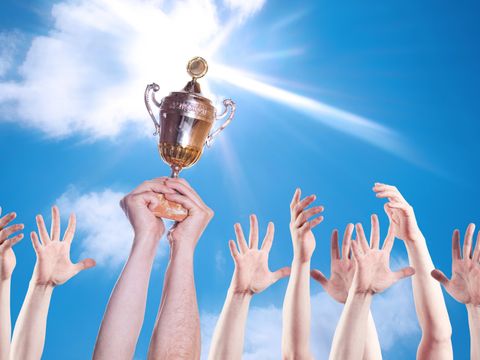 Hände mehrerer Personen mit einem Pokal